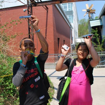 1 boy and 1 girl hold PV solar panels high up towards the sun, during a solar workshop
