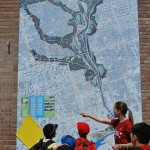 groups of students stand in front of a large map with an adult who is explaining details
